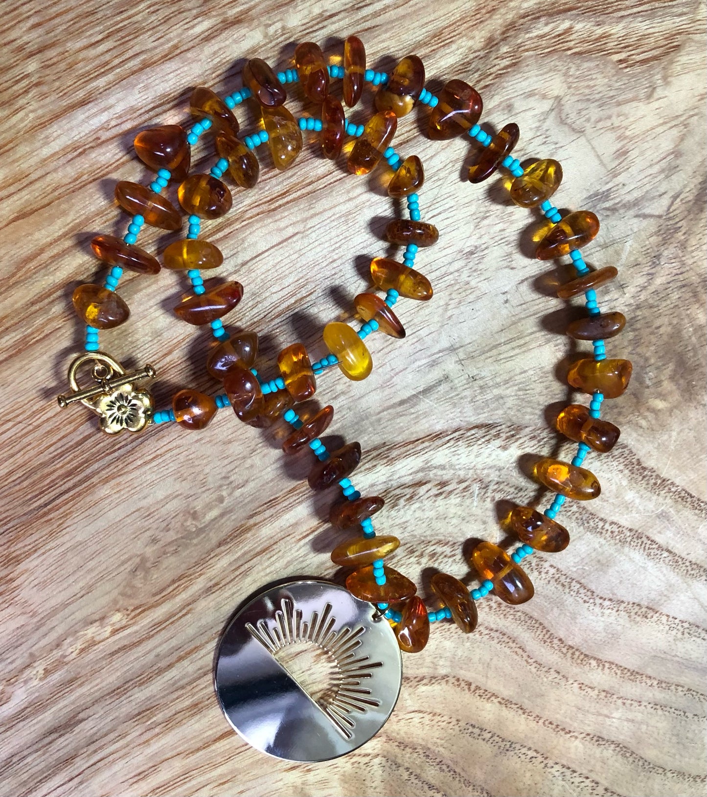 amber beaded necklace with turquoise glass seed beads and a gold plated sunrise pendant
