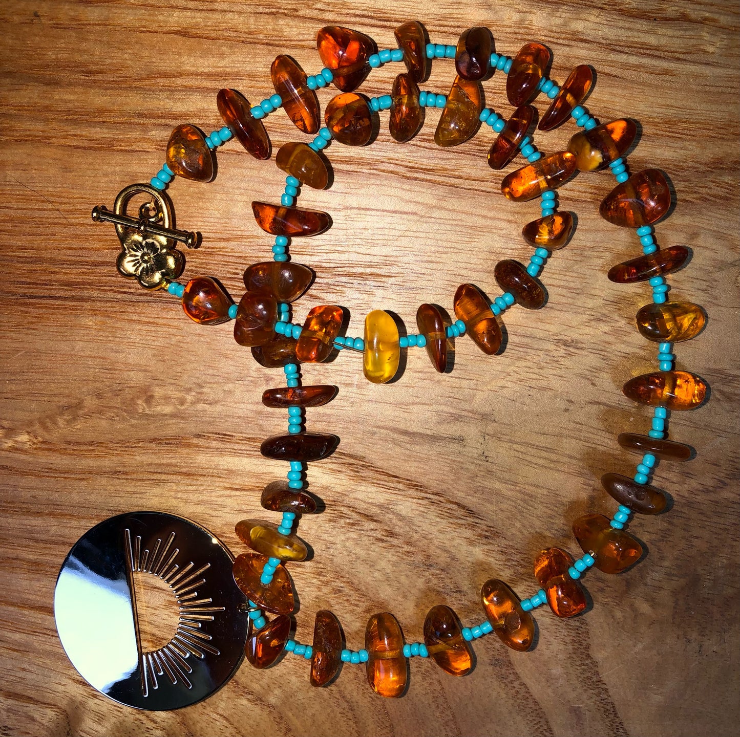 amber beaded necklace with turquoise glass seed beads and a gold plated sunrise pendant