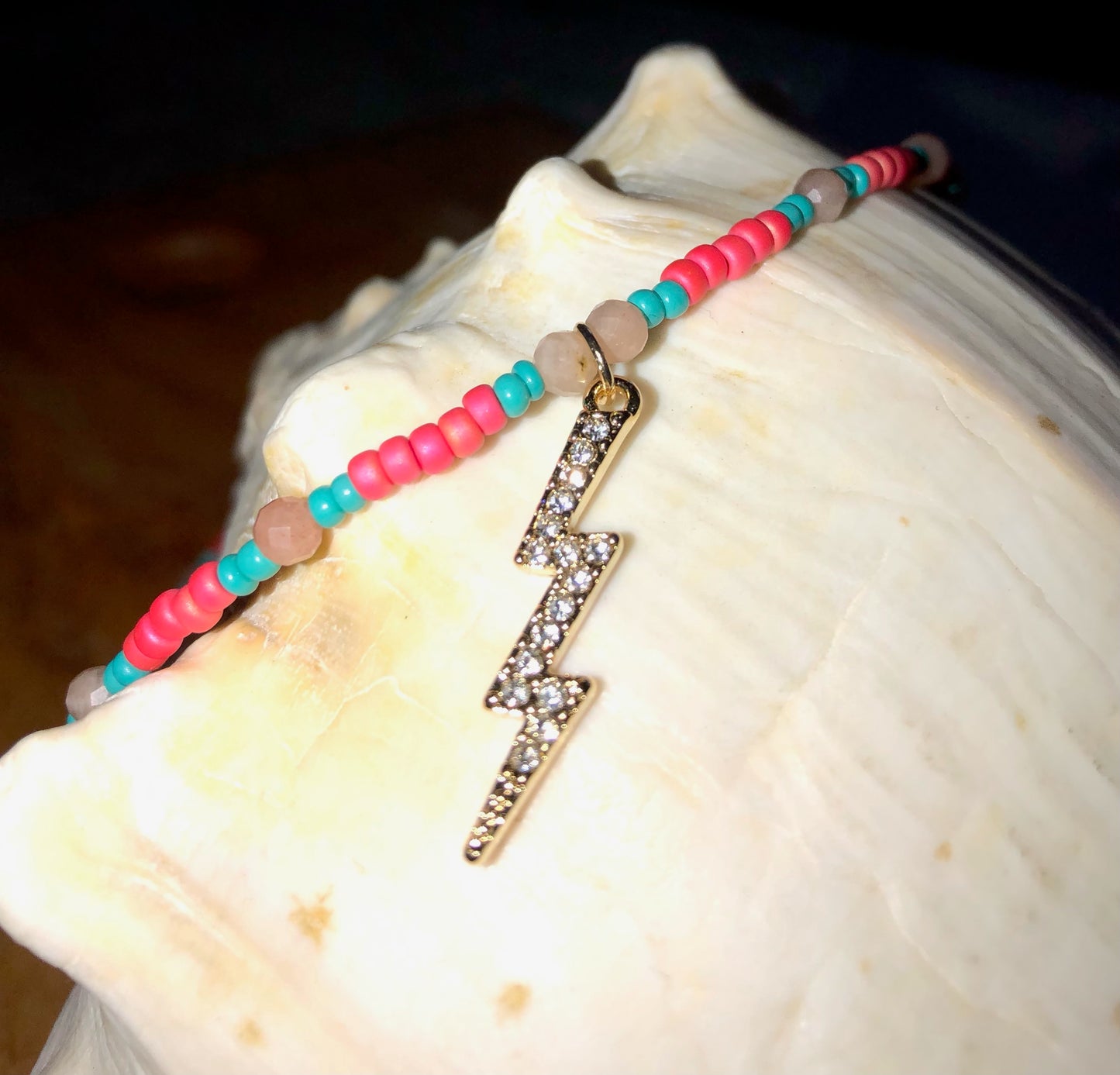 Necklace with a 29mm gold plated clear crystal lightning bolt charm, hot pink & turquoise glass seed beads, and peach sunstones.