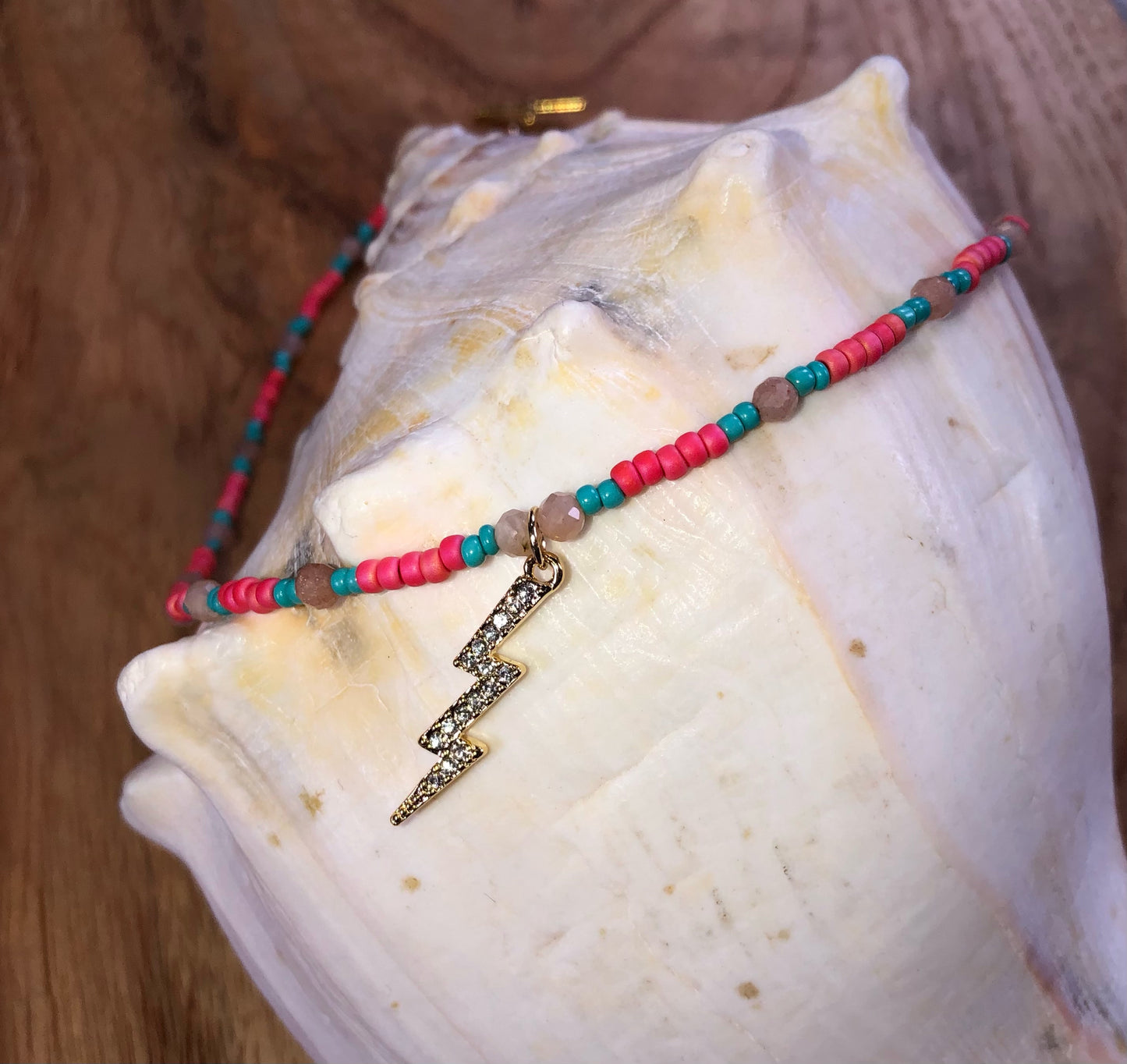 Necklace with a 29mm gold plated clear crystal lightning bolt charm, hot pink & turquoise glass seed beads, and peach sunstones.