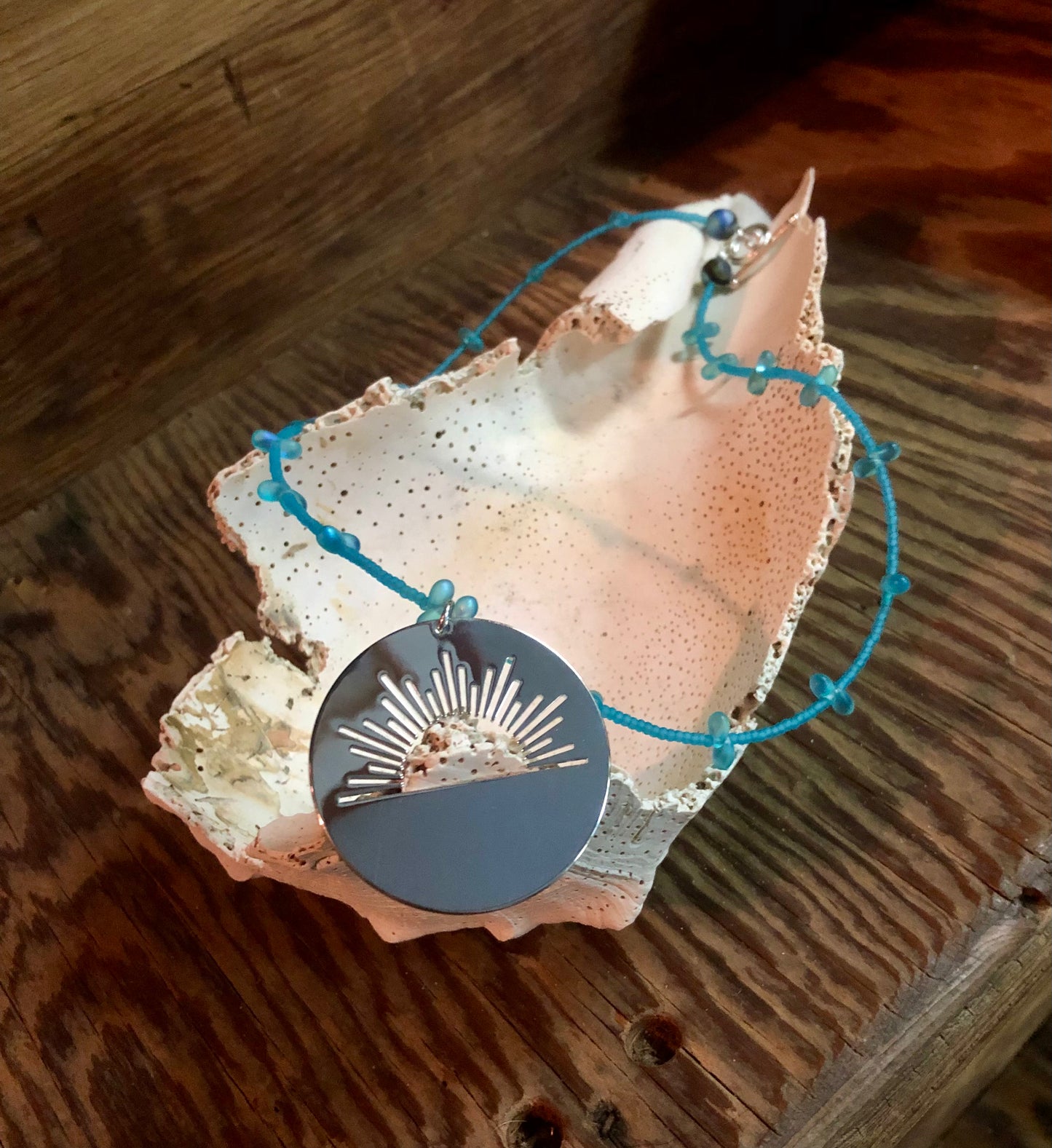 Silver plated sunrise charm necklace with blue Czech teardrop beads, and blue glass seed beads.