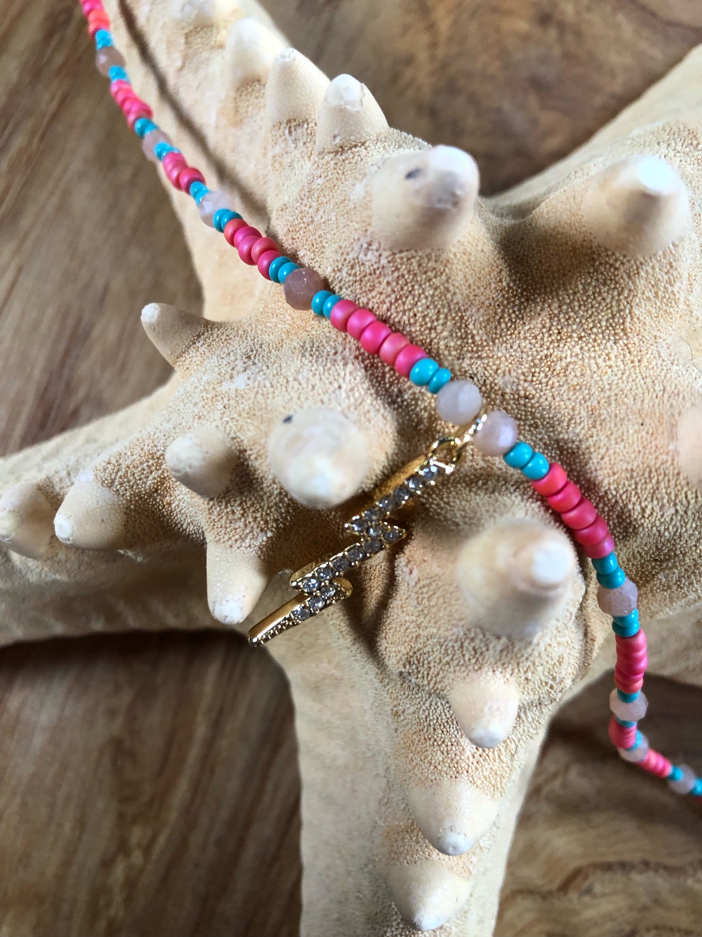 Necklace with a 29mm gold plated clear crystal lightning bolt charm, hot pink & turquoise glass seed beads, and peach sunstones.