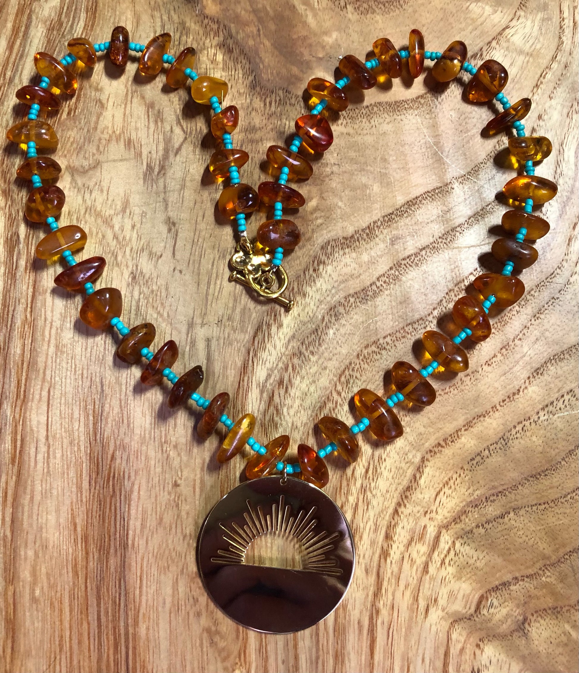 amber beaded necklace with turquoise glass seed beads and a gold plated sunrise pendant
