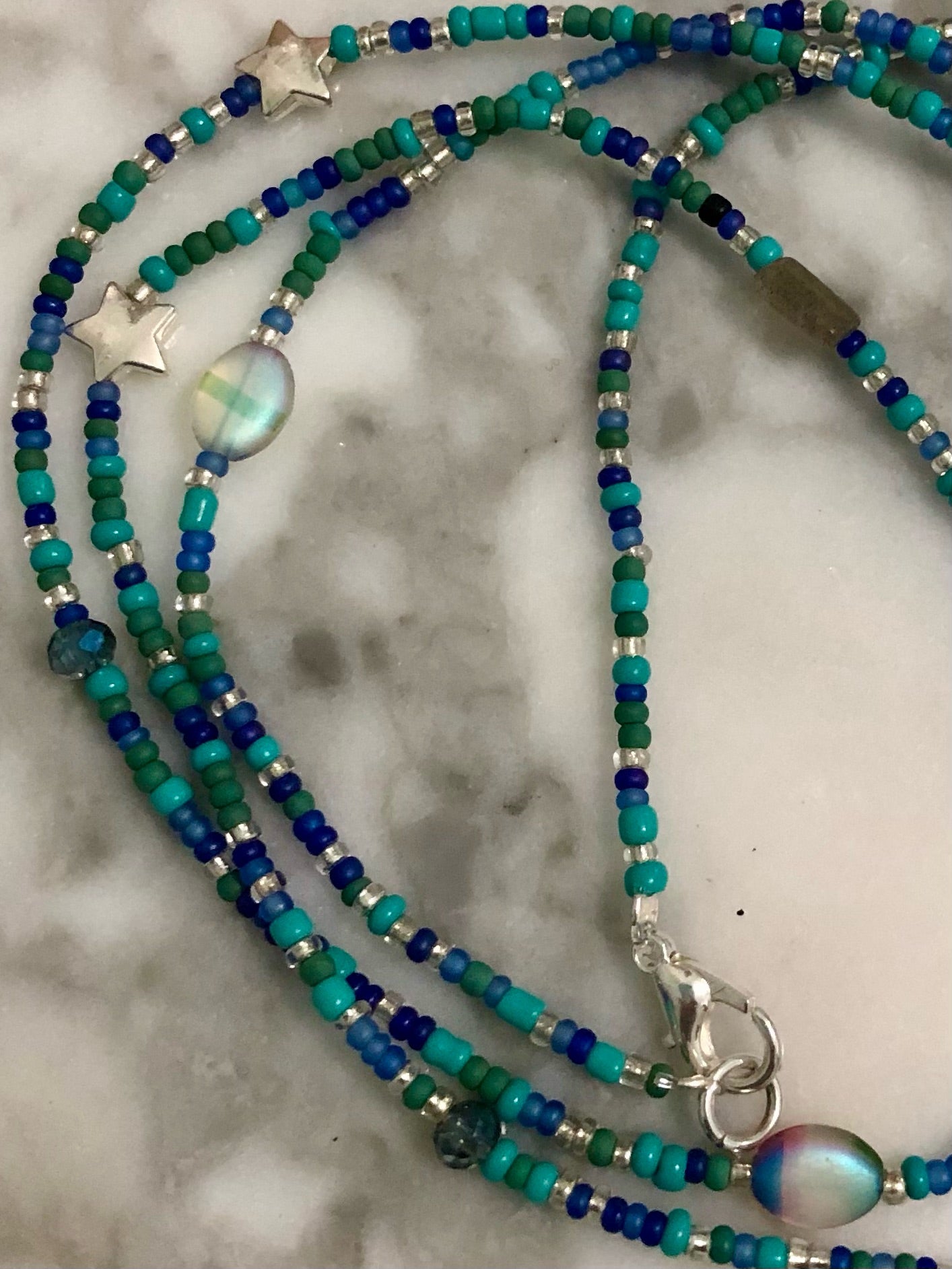 Waist beads in blue, green, and silver glass seed beads, silver plated star beads, multi-colored glass beads, and labradorite beads on elastic cord with a silver plated clasp.