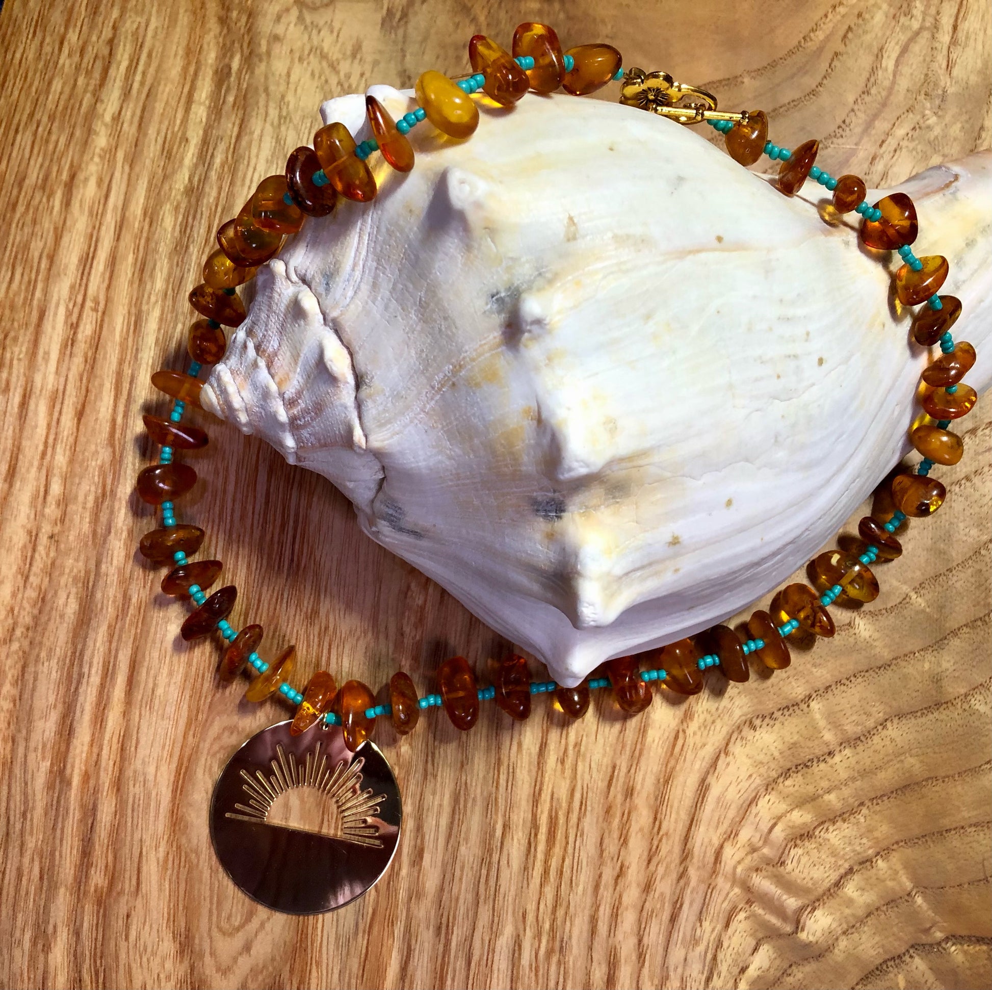 amber beaded necklace with turquoise glass seed beads and a gold plated sunrise pendant