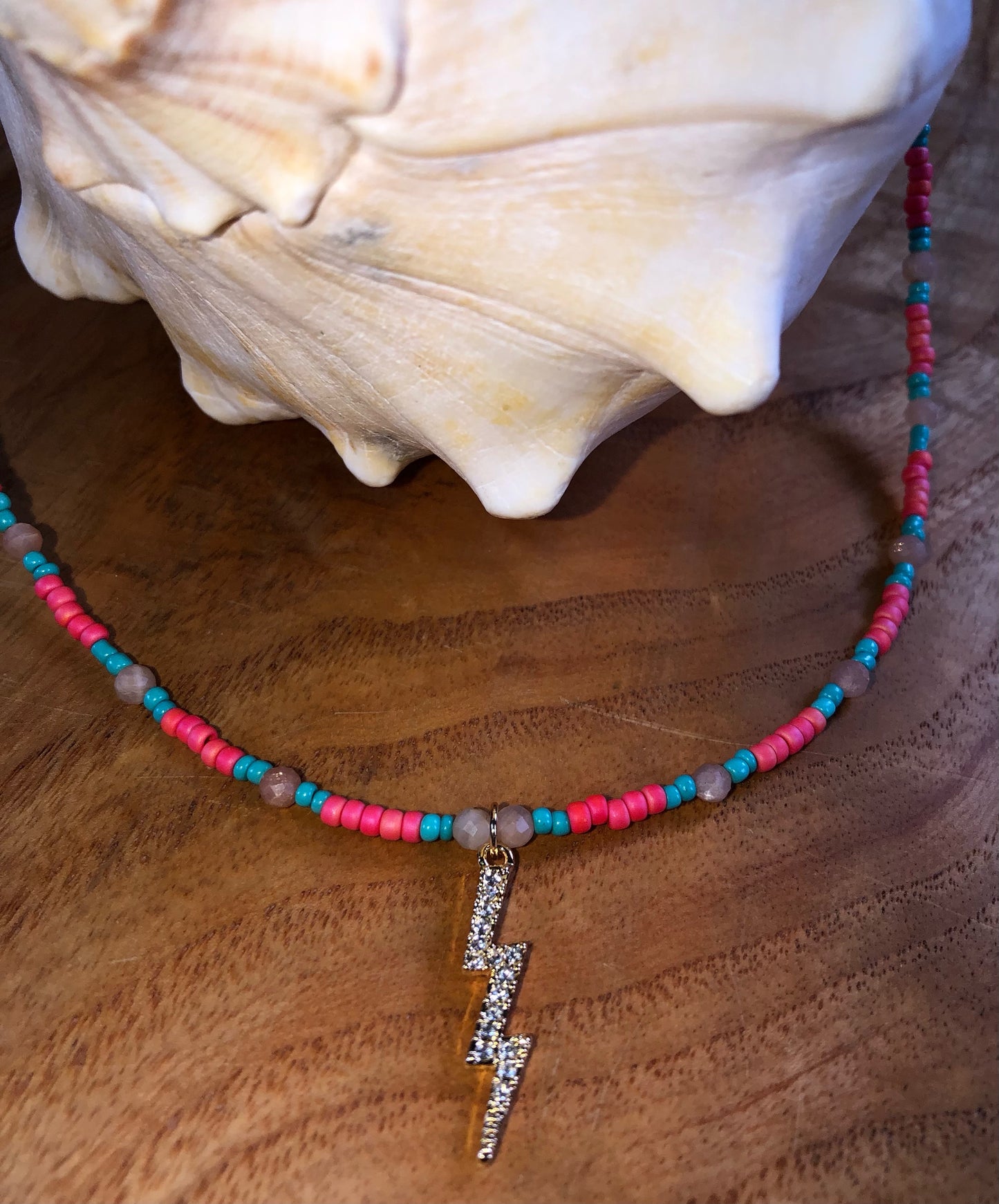 Necklace with a 29mm gold plated clear crystal lightning bolt charm, hot pink & turquoise glass seed beads, and peach sunstones.