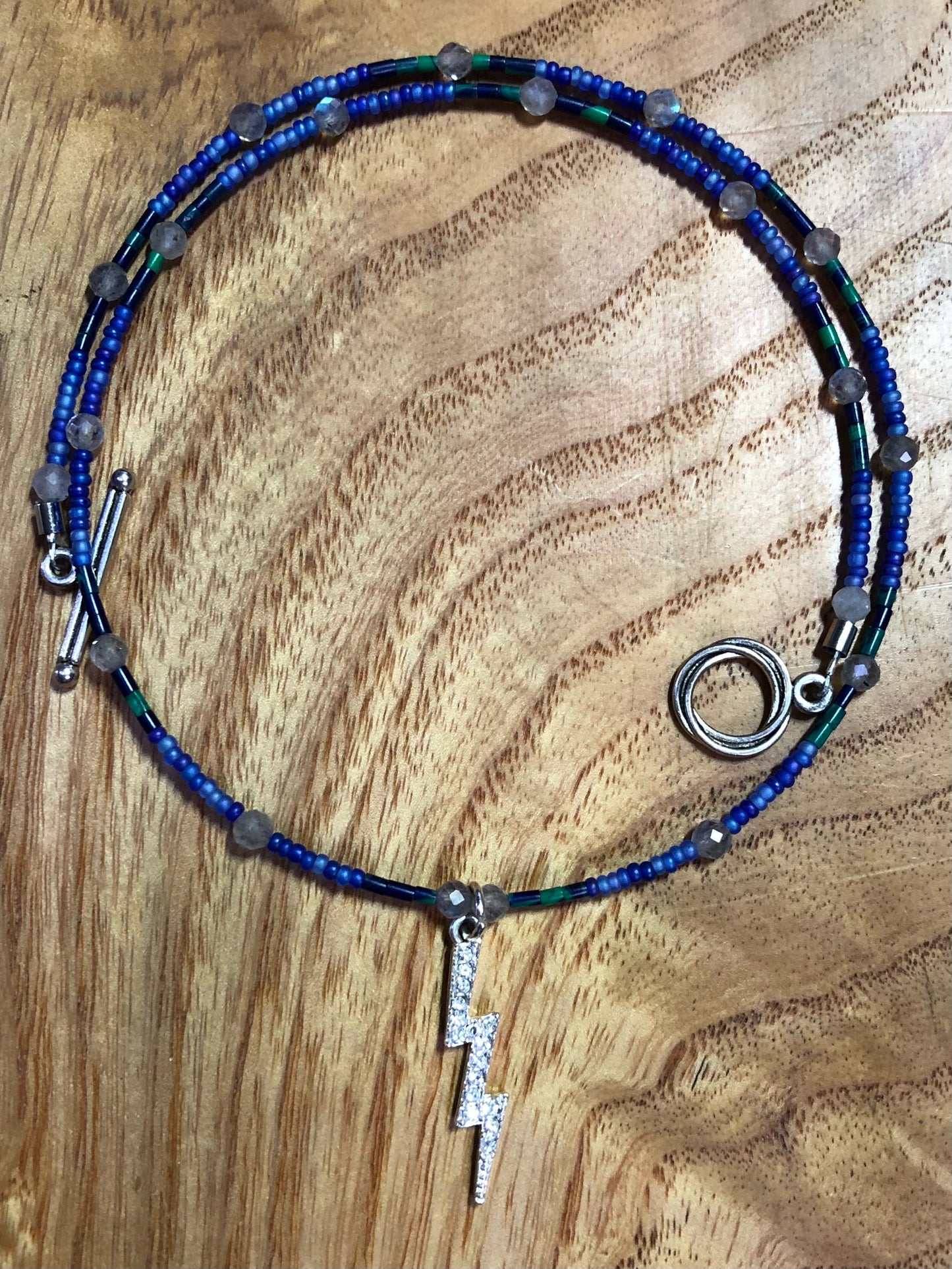 Necklace with 29mm silver plated with clear crystal lightning bolt charm, lapis and malachite tube beads, blue glass seed beads, and labradorite beads.